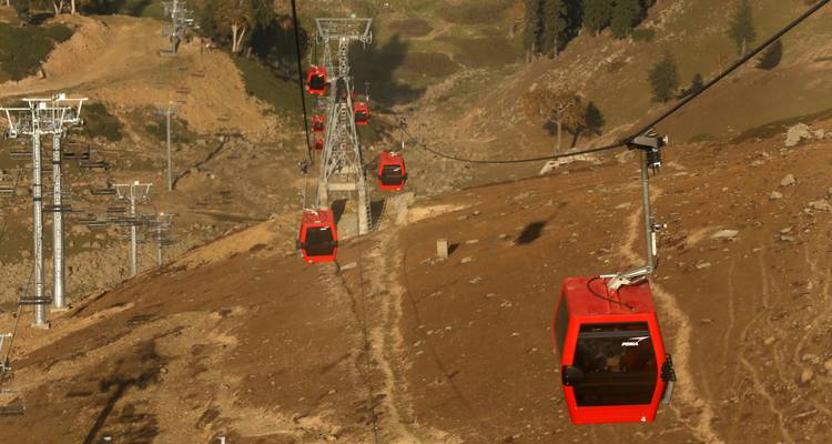 Des téléphériques rouges remontant une colline.