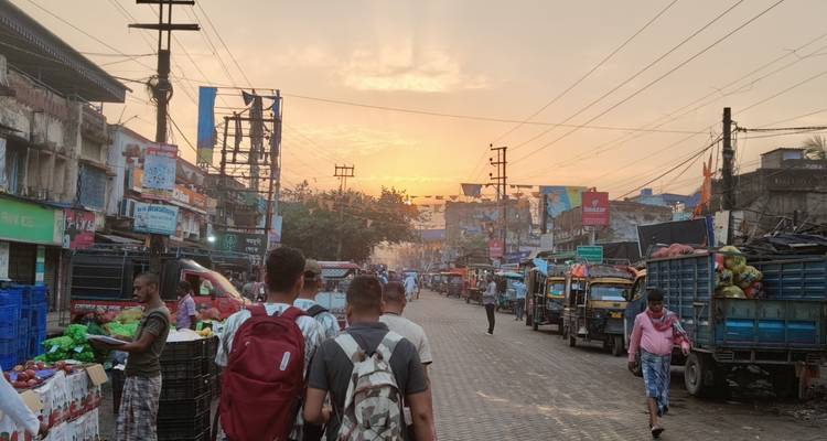 Bustling street market in Kolkata at sunrise with travelers carrying backpacks walking among stalls and tuk-tuks.