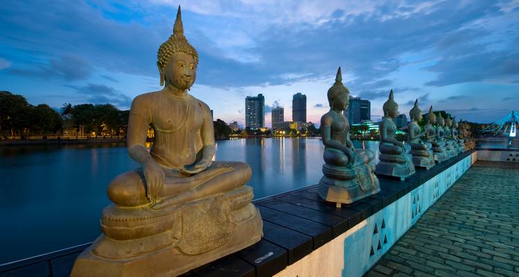 Buddha statues lined along a waterfront walkway during dusk.