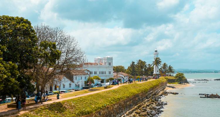 Coastal view with a lighthouse and people walking along a promenade.