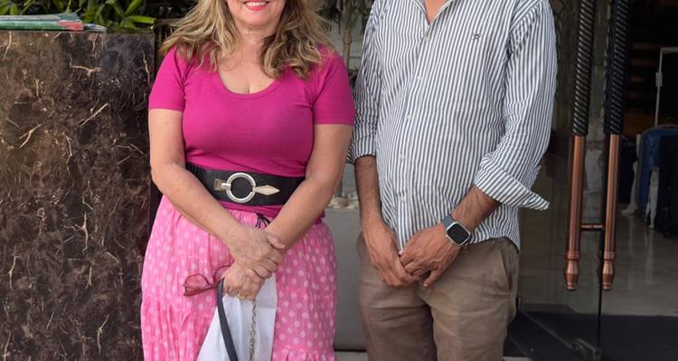 Twee mensen poseren voor een foto voor de ingang van een gebouw.