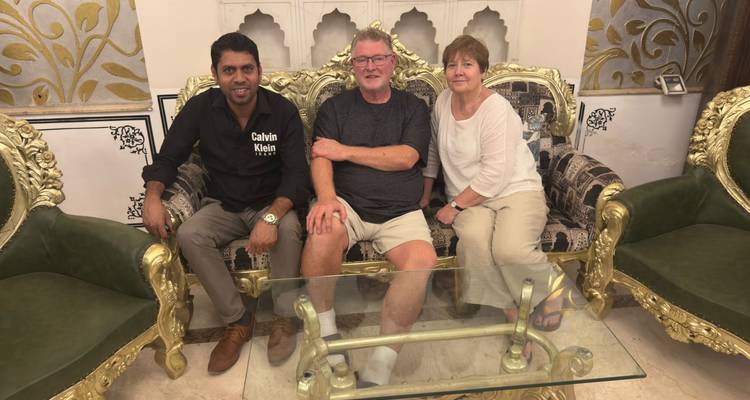 Drie mensen zitten op een luxueuze bank in een sierlijke kamer.