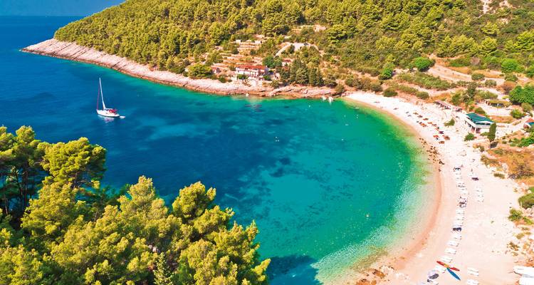 Abgelegener Strand in einer Bucht mit üppigem Grün und einem Segelboot.