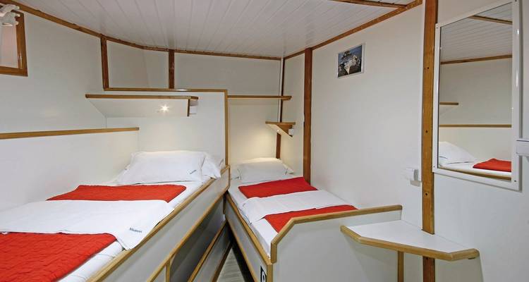 Kleines Hütteninterieur mit zwei Einzelbetten und Holzakzenten.