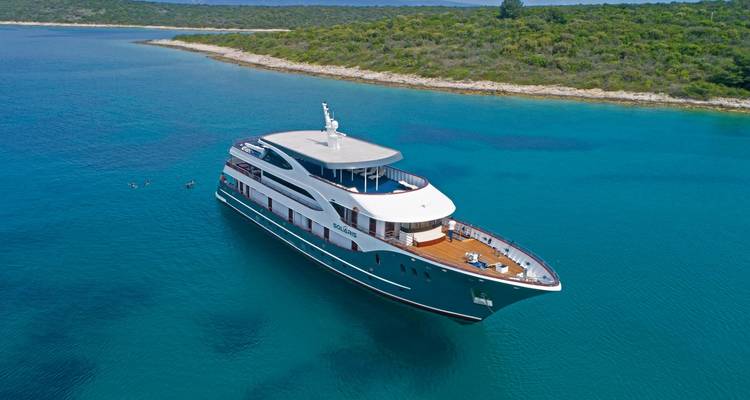 Luxusyacht vor Anker in klarem blauen Wasser nahe einer bewaldeten Küste.