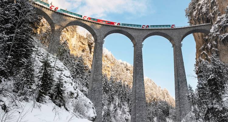 Train traversant un haut viaduc entouré de montagnes enneigées