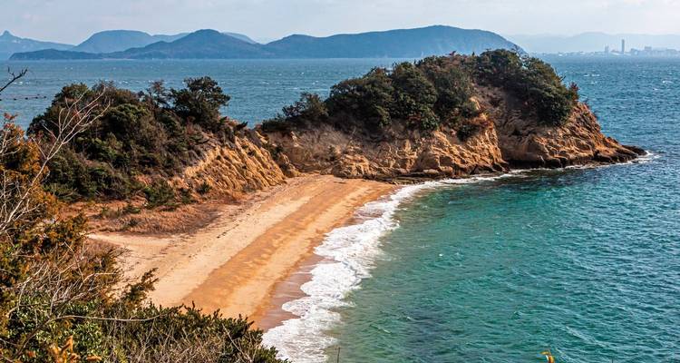 Coastal landscape with a rugged shoreline and distant mountains.