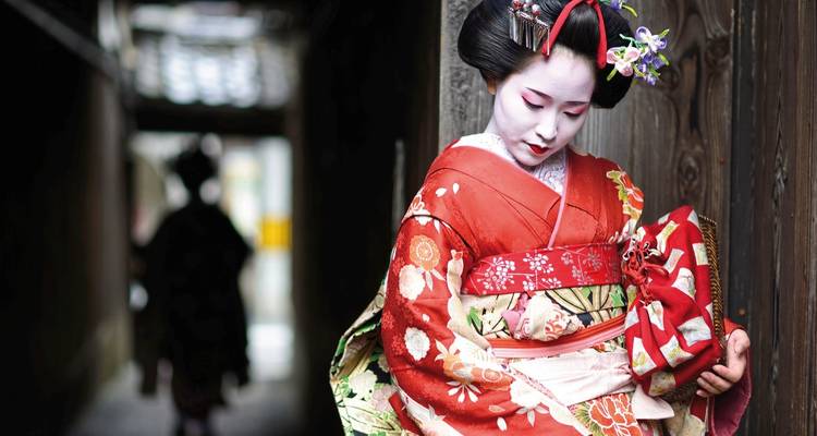 Eine Geisha in traditionellem Kimono in einer schmalen Gasse.
