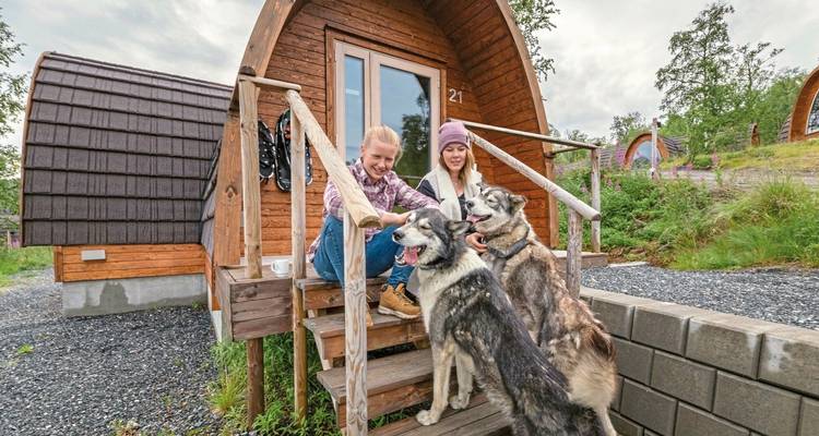 Deux personnes avec des chiens de traîneau devant une cabane en bois.