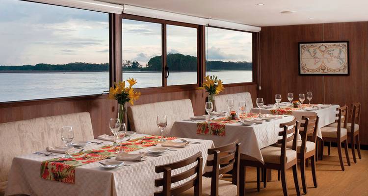 Un área de comedor con mesas puestas para una comida y vista al río.