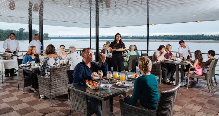 Personas cenando en la cubierta de un crucero con vistas al río.
