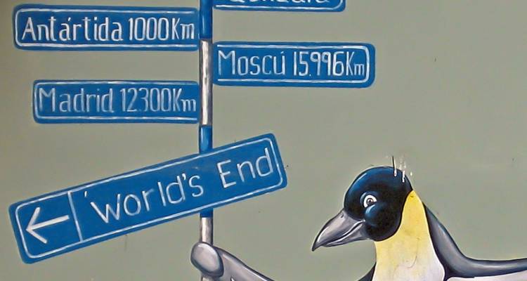Panneau indicateur avec distances vers diverses destinations, tenu par une peinture murale de pingouin.