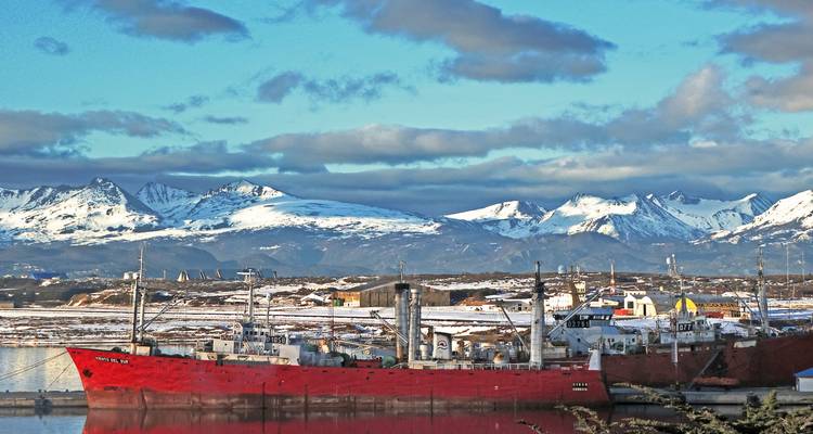 Des navires rouges amarrés près d'une ville avec des montagnes enneigées en arrière-plan.