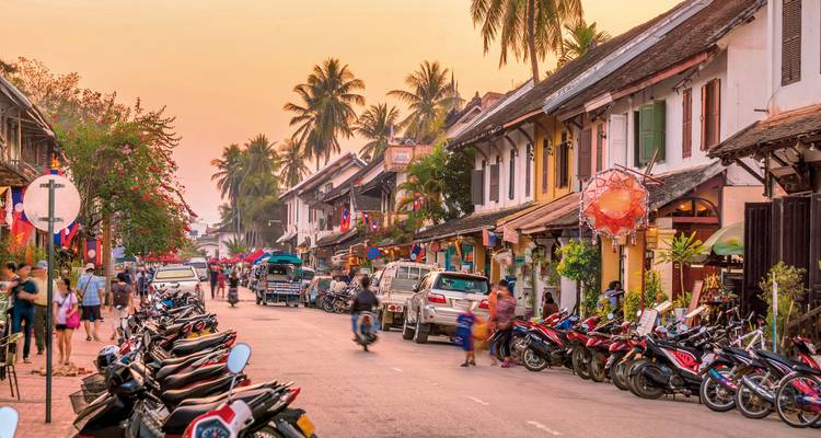 Een levendige straat in Luang Prabang met motorfietsen en mensen.