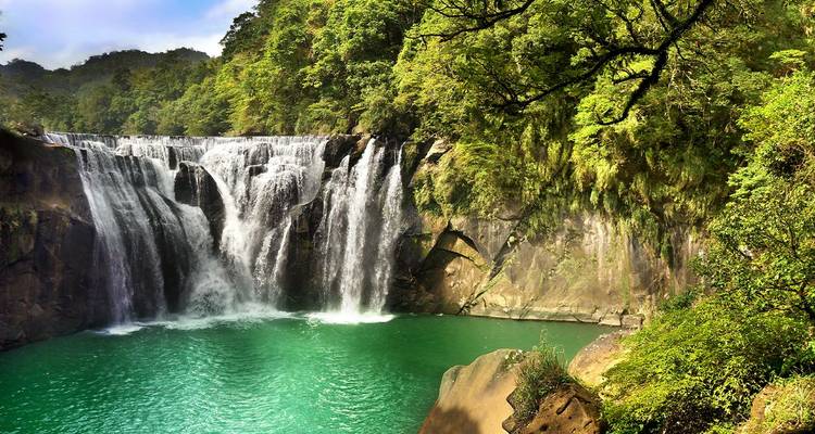 Una impresionante cascada de múltiples niveles que se desploma en una piscina de color esmeralda rodeada de densa selva