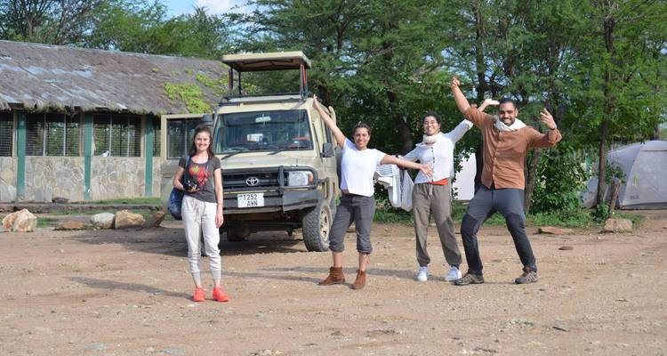 Group of people posing energetically near a safari vehicle.