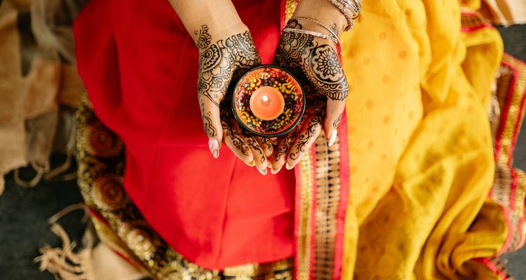 Hand adorned with henna holding a decorative candle.