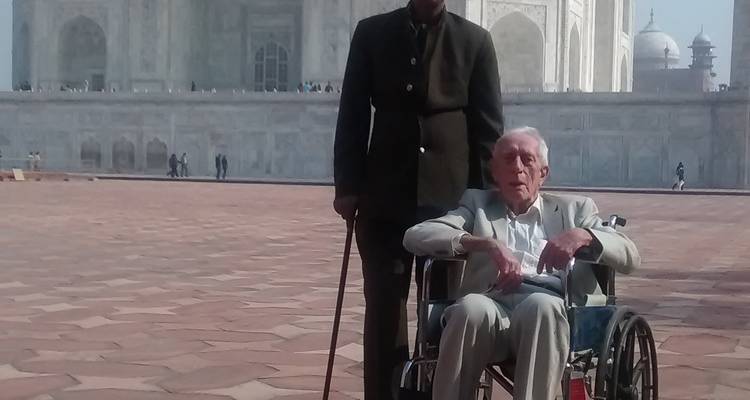 Two men in front of the Taj Mahal, one seated in a wheelchair.
