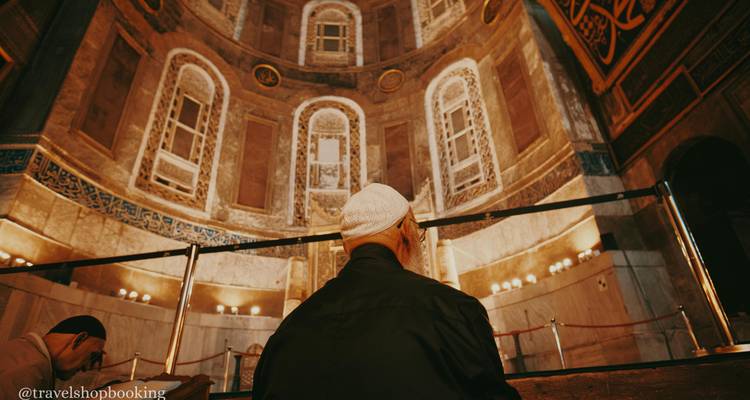 Mann mit Schädelkappe betet in einer reich verzierten Kuppelkammer, die von warmen Lichtern erleuchtet wird.