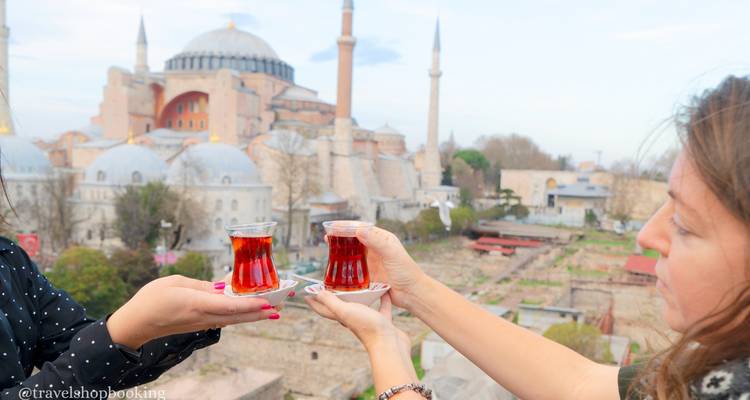 Zwei Frauen stoßen mit Tulpengläsern türkischen Tees an, mit der Hagia Sophia im Hintergrund.