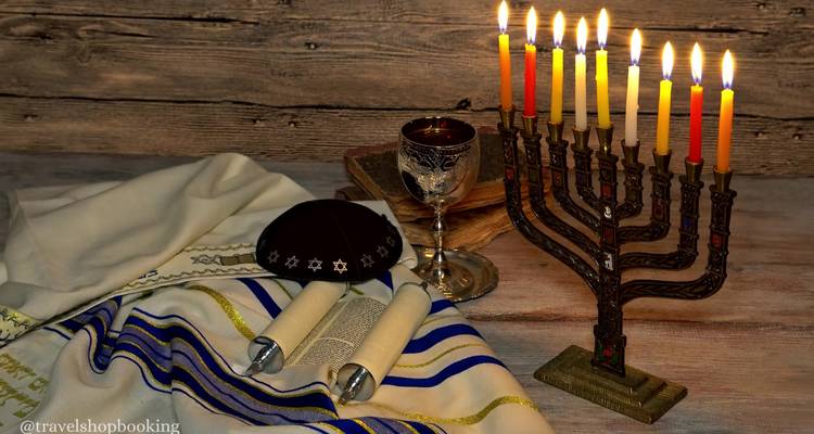 Chanukka-Menora mit brennenden Kerzen neben Kiddusch-Becher und Torarollen auf einem rustikalen Tisch.