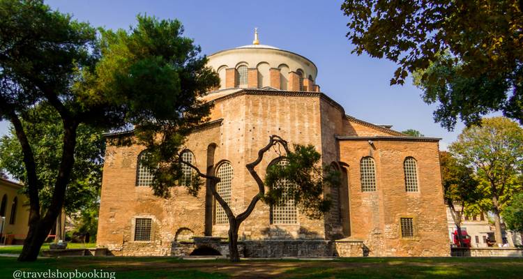Steinernes Äußeres der historischen Hagia-Irene-Kirche, eingerahmt von belaubten Bäumen unter klarem Himmel.