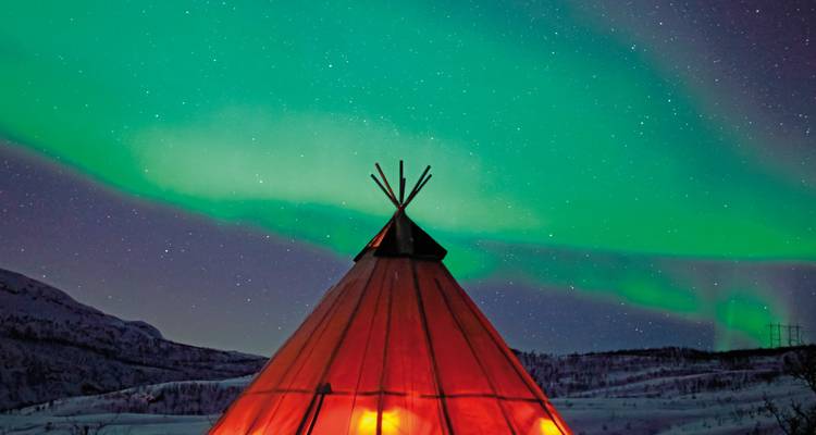 Noorderlicht boven een traditionele Sami tent in een besneeuwd landschap.