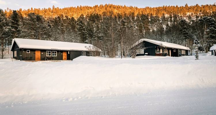 Houten hutten in een besneeuwde bos tijdens zonsondergang.