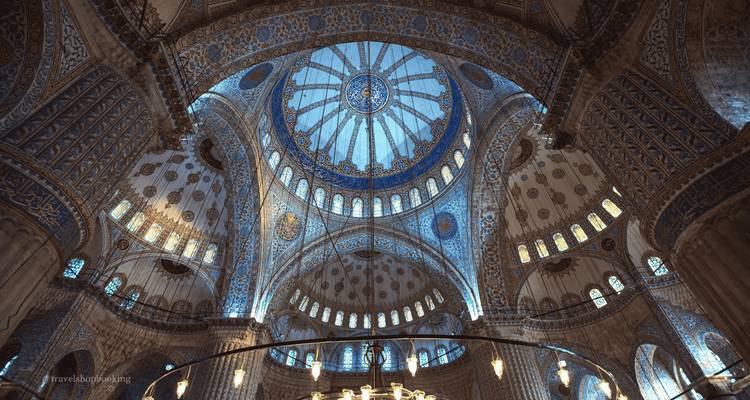 Verzierte blau geflieste Innenkuppel einer prächtigen Moschee mit gemusterten Bögen und Buntglasfenstern.