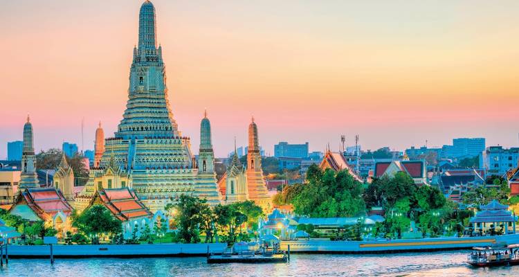 Wat Arun à Bangkok au bord de la rivière au coucher du soleil avec ses structures illuminées.