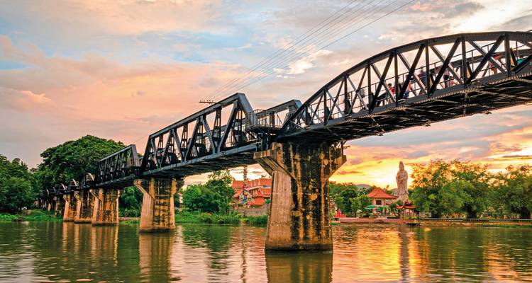 Pont ferroviaire en fer au-dessus d'une rivière avec un coucher de soleil en arrière-plan.