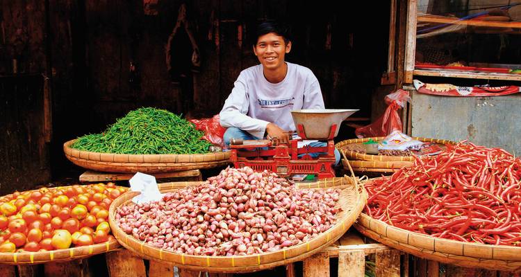 Scène de marché avec un vendeur et des produits colorés assortis.