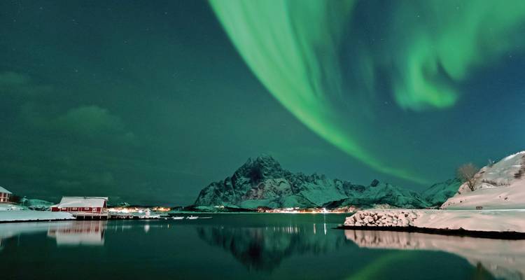 Spectacle dramatique d'aurores boréales au-dessus d'un paysage enneigé avec de l'eau reflétant les couleurs.