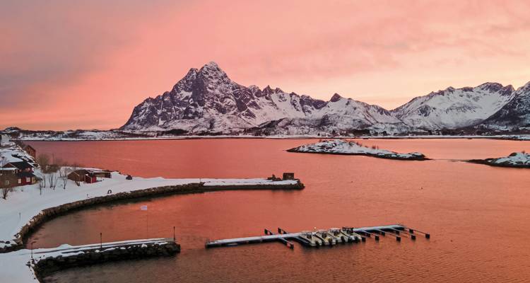 Coucher de soleil sur une chaîne de montagnes enneigées se reflétant dans des eaux glacées.
