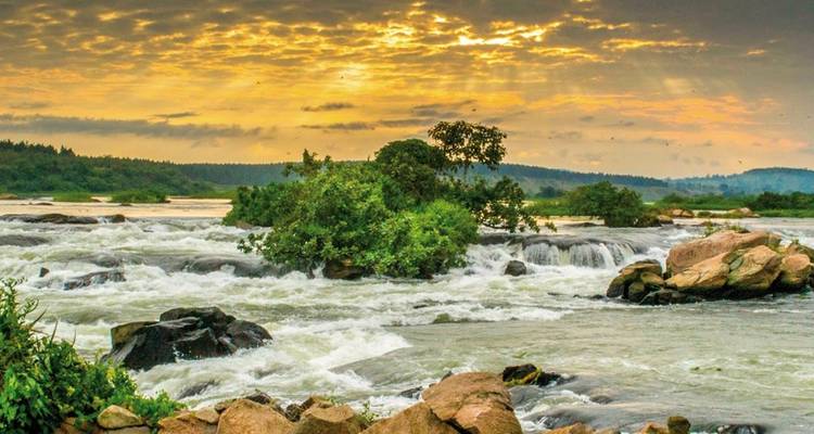 Waterval die over rotsen stroomt met weelderig groen onder een levendige hemel.