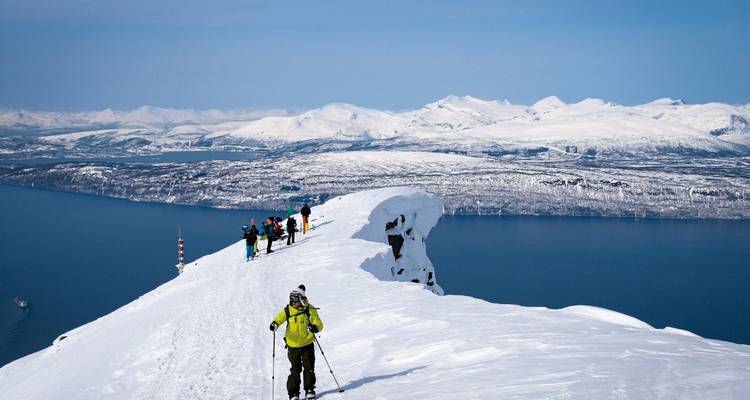 Des personnes faisant du ski le long d'une crête enneigée avec vue sur l'océan.