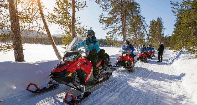 Gruppe von Menschen, die mit Schneemobilen durch einen verschneiten Wald fahren.