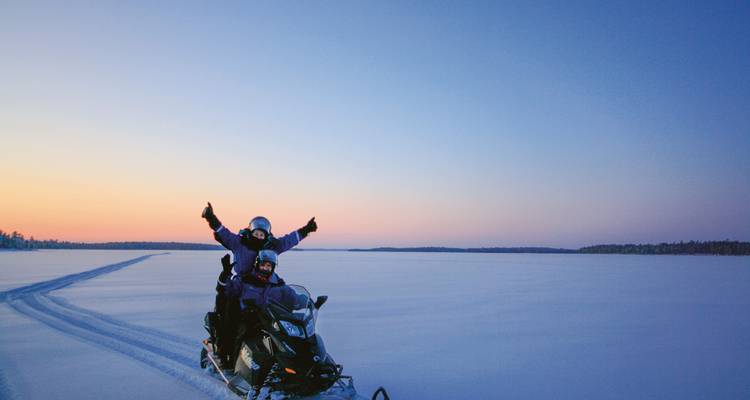 Person auf einem Schneemobil in einer verschneiten Landschaft bei Sonnenuntergang.