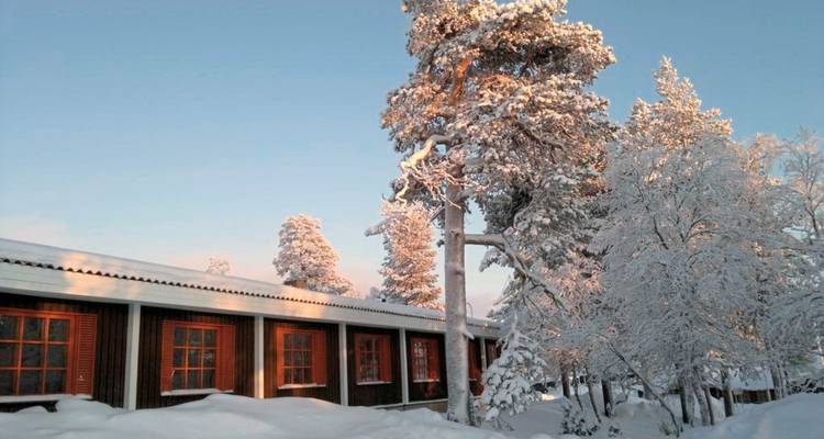 Cabane enneigée avec des arbres reflétant les lueurs du coucher de soleil.