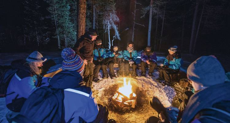 Un groupe de personnes assises autour d'un feu de camp dans la neige la nuit.