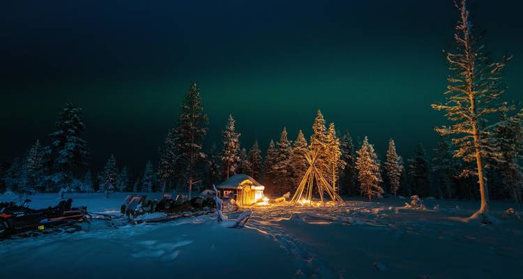 Campingplatz in einem verschneiten Wald mit Nordlichtern darüber.