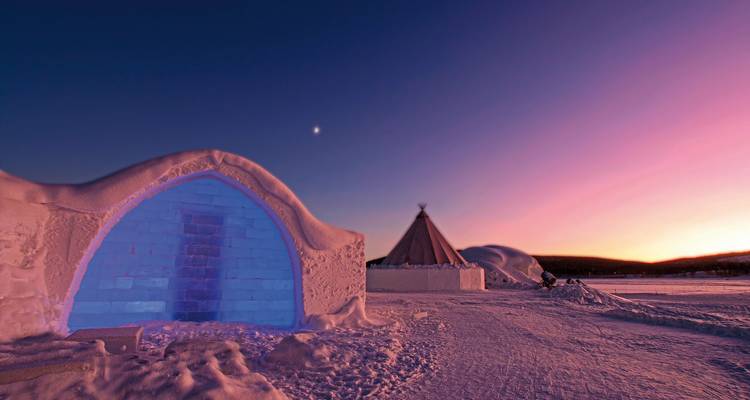 Igloo and teepee under a twilight sky, with snow on the ground.