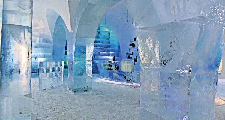 Interior of an ice building with large ice pillars and colorful lighting.
