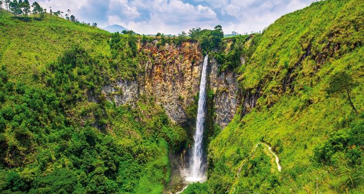 Waterfall surrounded by lush green cliffs.