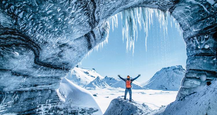 Personne qui pose à l'intérieur d'une grotte de glace avec des stalactites de glace.