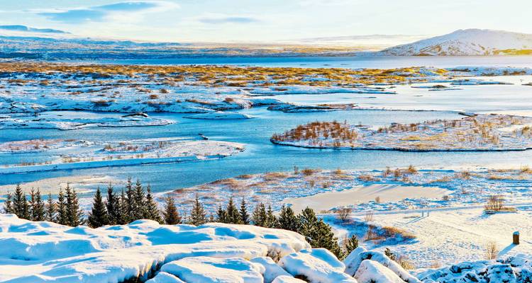 Vue enneigée de lacs gelés et d'îles bordés de conifères sous un soleil hivernal éclatant.
