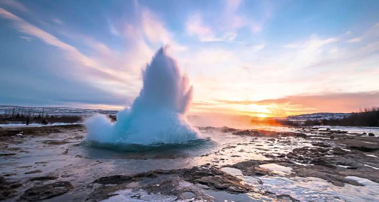 Géiser erupcionando al amanecer con vapor iluminado por el cielo colorido en el campo geotérmico de Islandia.