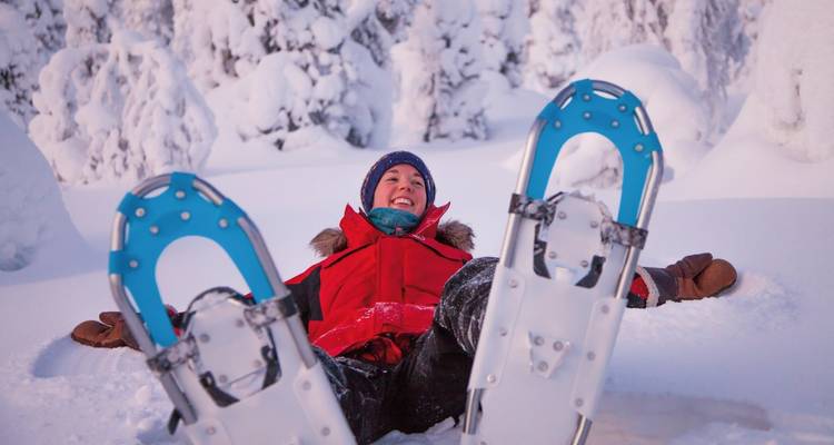 Personne en équipement d'hiver couchée joyeusement dans la neige avec des raquettes.