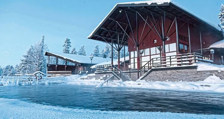 Refugio cubierto de nieve junto a un lago helado bajo un cielo azul pálido.