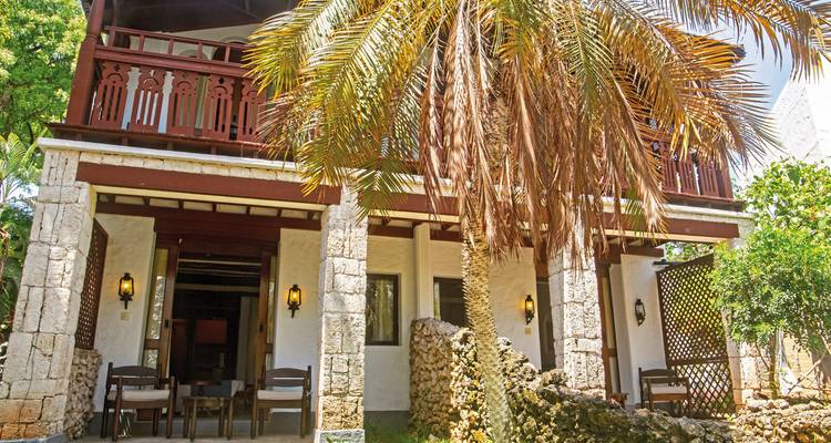 Front of a small hotel building with a palm tree.